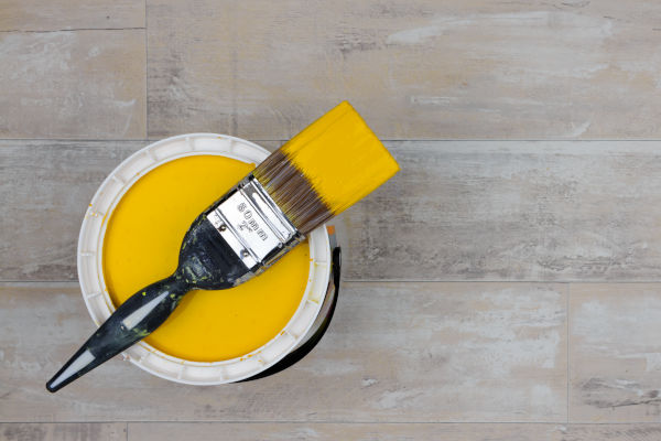 Paintbrush across an open can of bright yellow paint